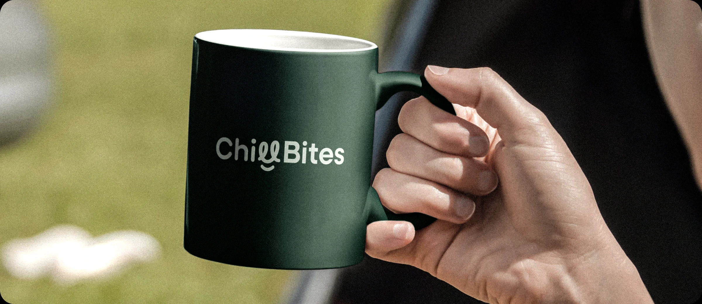 A hand holding a dark green ChillBites mug outdoors